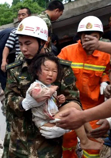 Một em bé mình mẩy xây xát và dính máu được nhân viên cứu hộ bế ra khỏi đống đổ nát ở Nhã An.