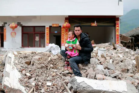 Một người đàn ông và một đứa trẻ ngồi trên đống đổ nát của ngôi nhà sau trận động đất tại làng Wuxing, thị xã Long Môn, huyện Lô Sơn, tỉnh Tứ Xuyên hôm 11/4.