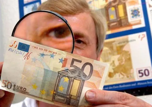 Một chuyên gia đang soi kiểm tra tờ tiền 50 Euro bị nghi ngờ là giả