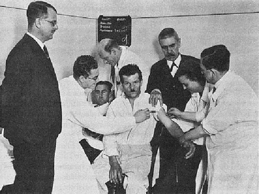 Bác sĩ Wagner (áo đen ở giữa) đang xem một bệnh nhân được tiêm vi khuẩn sốt rét vào người năm 1934