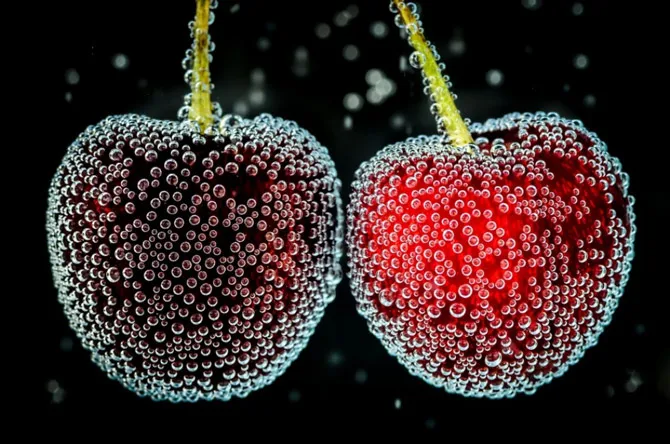 Hai trái cherry bám đầy bong bóng li ti khi ngâm trong ly rượu.