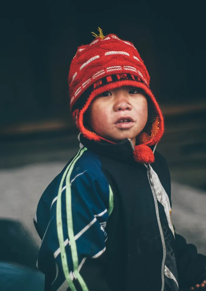 Một em bé có gương mặt lấm lem với chiếc áo khoác mỏng đang đi lại trên đường .