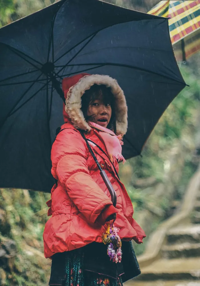 Bé gái này có trang phục ấm áp hơn với chiếc áo phao, trời mưa khiến các em phải dùng ô khi ra ngoài đường