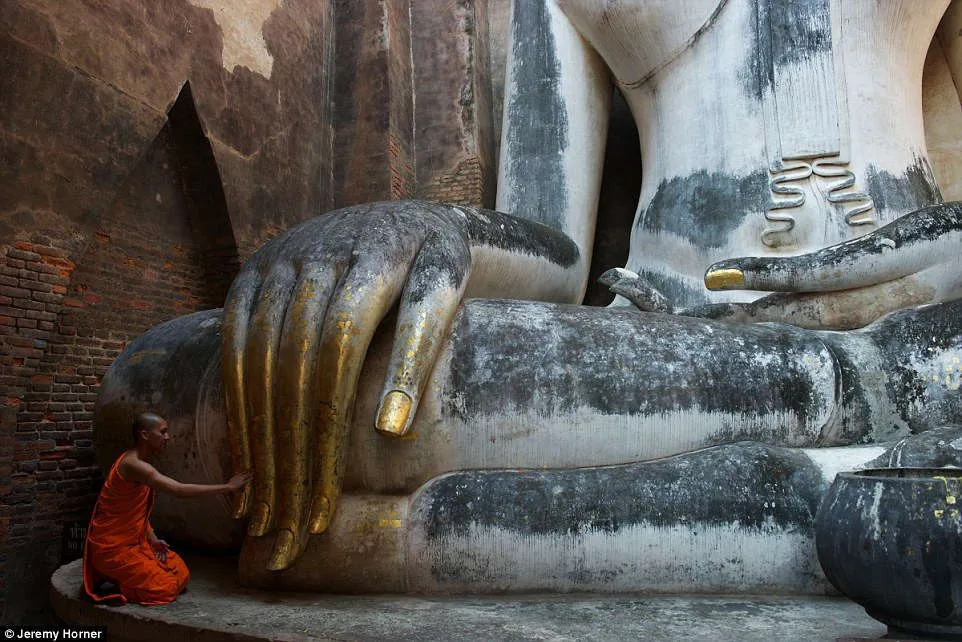 Một nhà sư chạm tay vào bức tượng Phật khổng lồ tại chùa Wat Si Chum, Thái Lan.