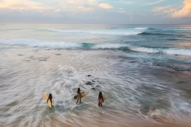 Tại bãi biển Makaha ở Oahu, Hawaii, hai chị em ruột cùng một người em họ chạy trên những con sóng để làm nóng người trước khi tham gia cuộc thi lướt sóng.