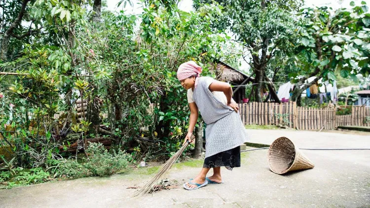 Một người phụ nữ đang quét rác vào giỏ rác hình phễu tại làng Mawlynnong.