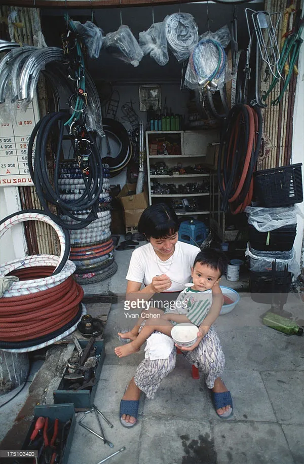Người phụ nữ bón cho con ăn bên ngoài một cửa hàng phụ tùng xe đạp.